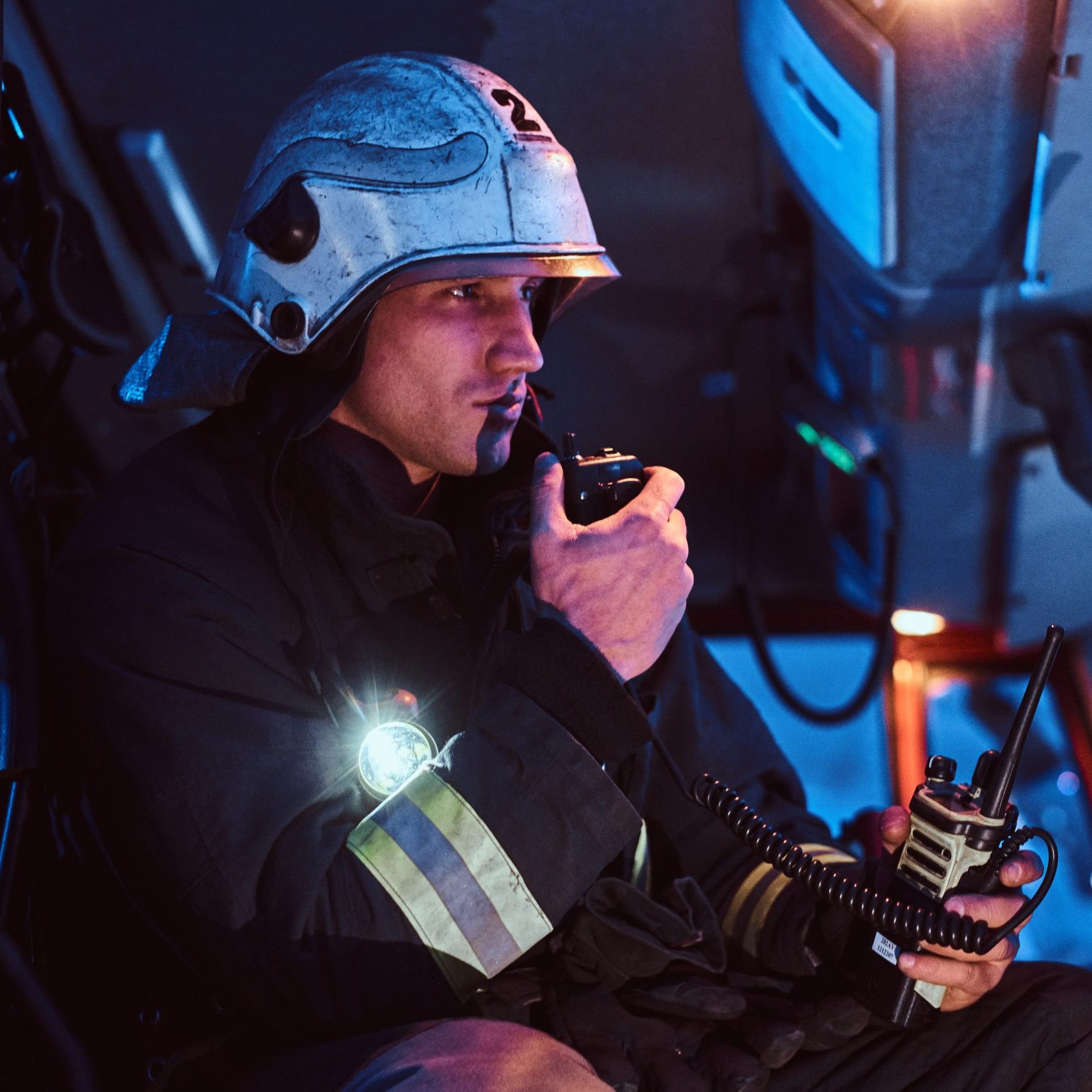 The fire brigade arrived at the night-time. Fireman in a protective uniform sitting in the fire truck and talking on the radio