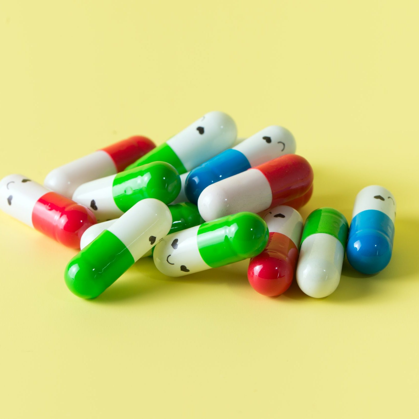 Pile of supplement capsules or drugs with smiling face over yellow background